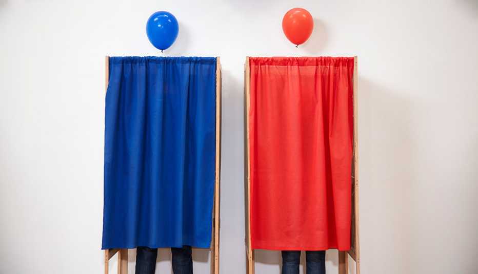 Voters voting in polling place, one in a blue booth and one in a red booth