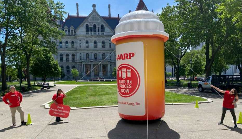 a a r p volunteers hold up a giant inflatable pill bottle with signs advocating for fair drug prices now