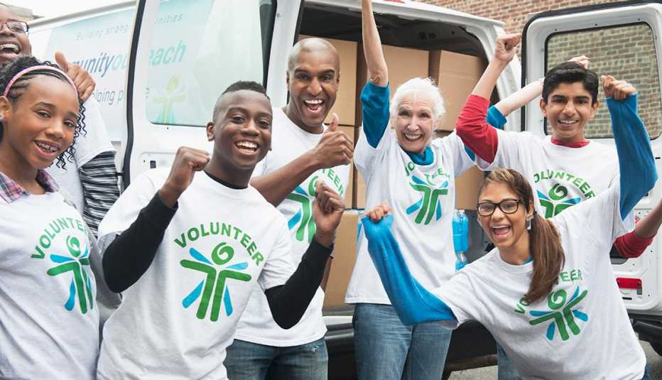 An enthusiastic group of community outreach volunteers  are cheering  in a posed photograph outside of their delivery van.  