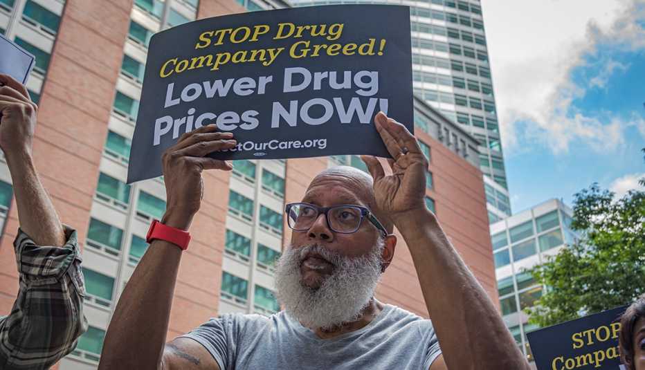 a man holds a sign that reads stop drug company greed, lower drug prices now, during a protest outside the jones day offices in manhattan