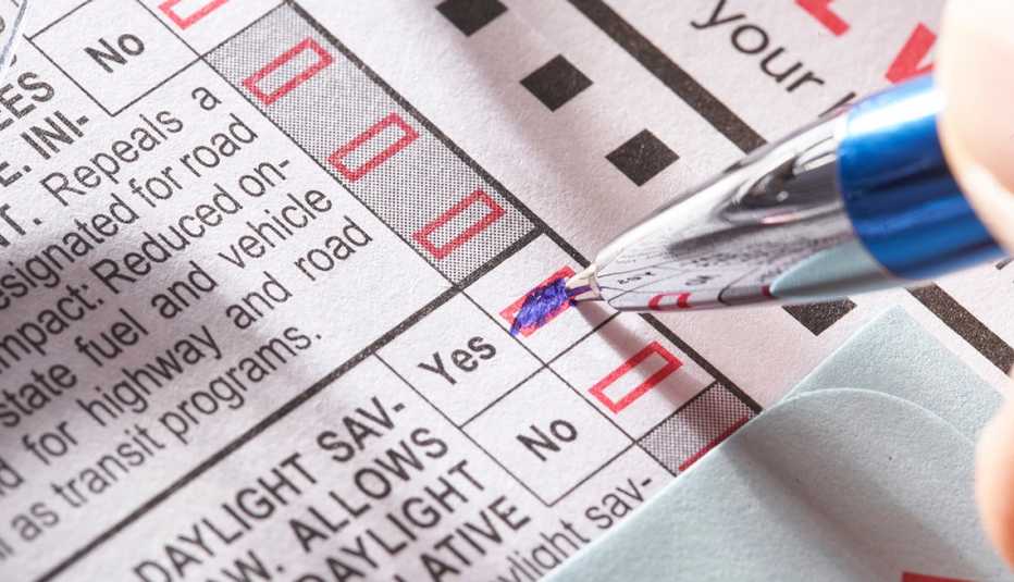 A person colors in a yes box on a ballot with a blue pen