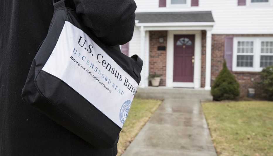 close up of a shoulder bag with census logo as worker approaches front door of home