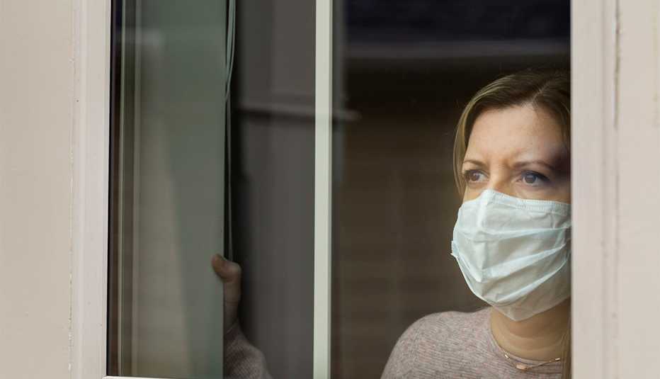A masked woman in quarantine looks out the window of her home.