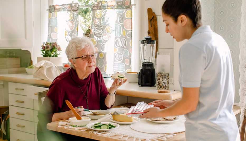An in home care worker showing medications to a woman as she eats at her kitchen table