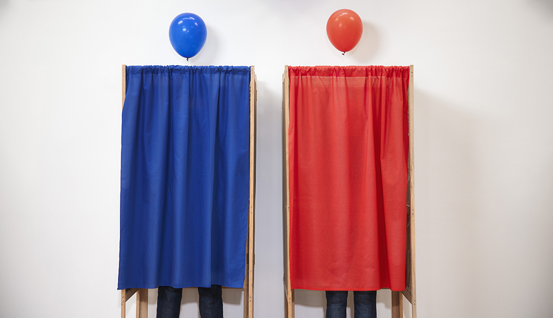 Voters voting in polling place, one in a blue booth and one in a red booth