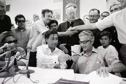 Hands of a grower and a farm worker clasp in the background, as César Chávez (l) of the United Farm Workers (UFW) union and John Giumarra Sr., representing 26 of California's largest table grape growers, exchange pens to sign a contract with the UFW on July 29, 1970, in Delano, California. Chávez's UFW has pushed a boycott on table grapes for the past five years. With this signing, the UFW now has contracts with 85 percent of the table grape growers.