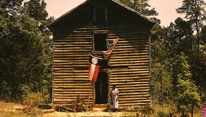 An unidentified Negro woman stands  in front of a building with the Georgia State flag and the United States flag.
