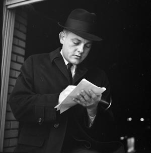 Bob Schieffer, dressed in a suit and hat, writes notes during his time as a crime reporter