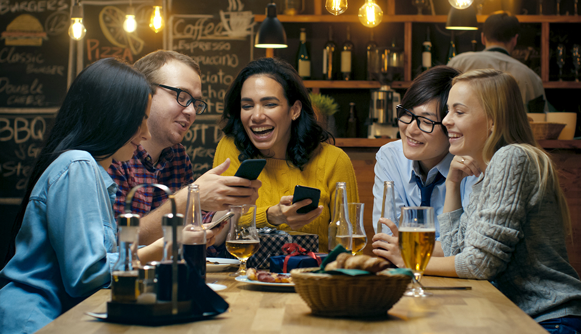 group of younger people in a bar, laughing and looking at phones
