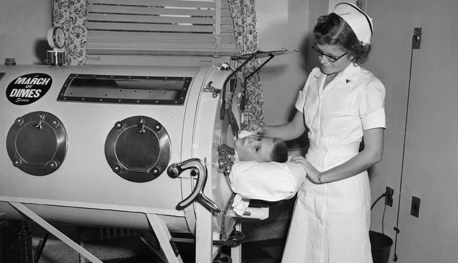A nurse stands next to an iron lung