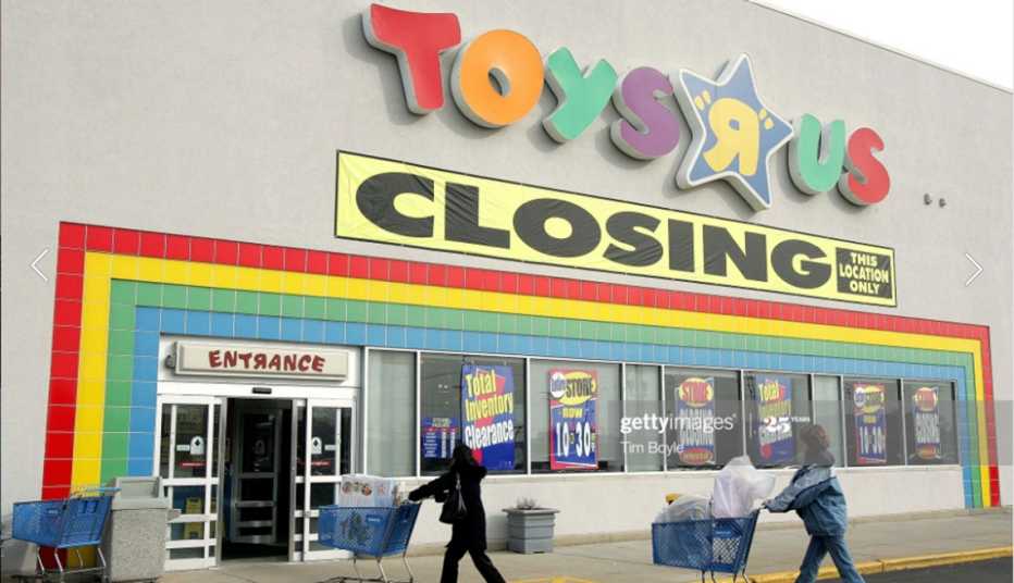 the front of a toys r us store showing its sign with a large closing sign under it and two shoppers walking in with carts
