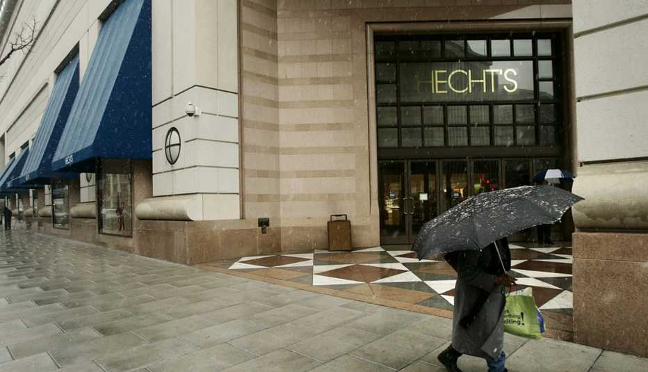 a rainy day street scene of a shopper hidden under an umbrella rushing past a hechts department store