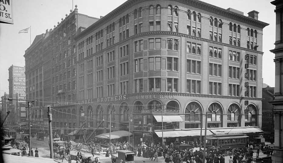 old black and white photo taken from across an intersection on a roof or through a high level window of a gimbels department store building on a city street showing people and horse drawn carriages in the street