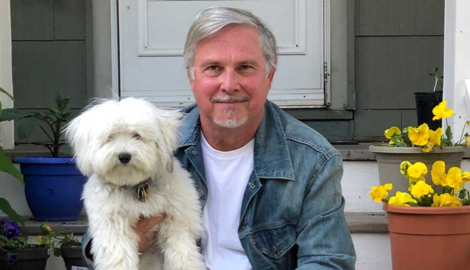 Crocker Stephenson sostiene a su perro mientras está sentado en el porche de su casa