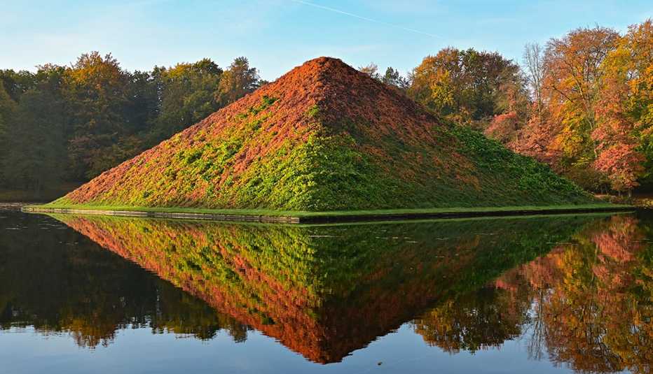 sun shines on lake pyramid which is shades of green and orange; trees behind pyramid and water in front