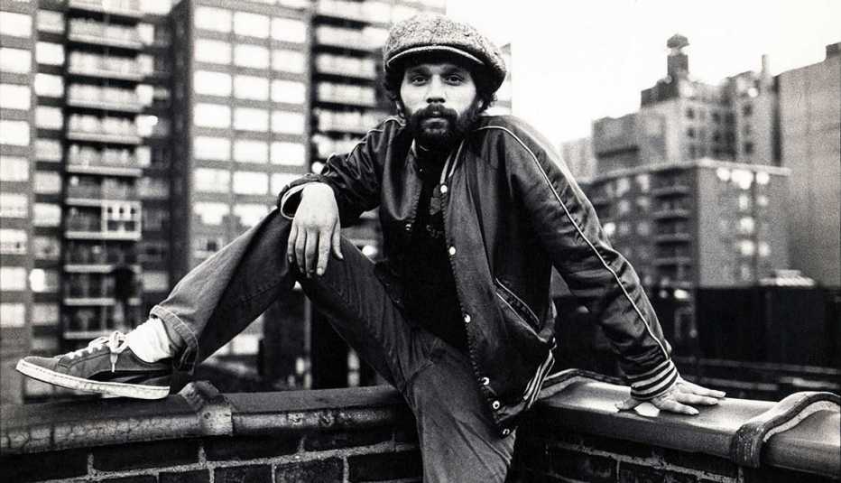 Miguel Piñero sits on the rooftop of a building with the New York City skyline in the background