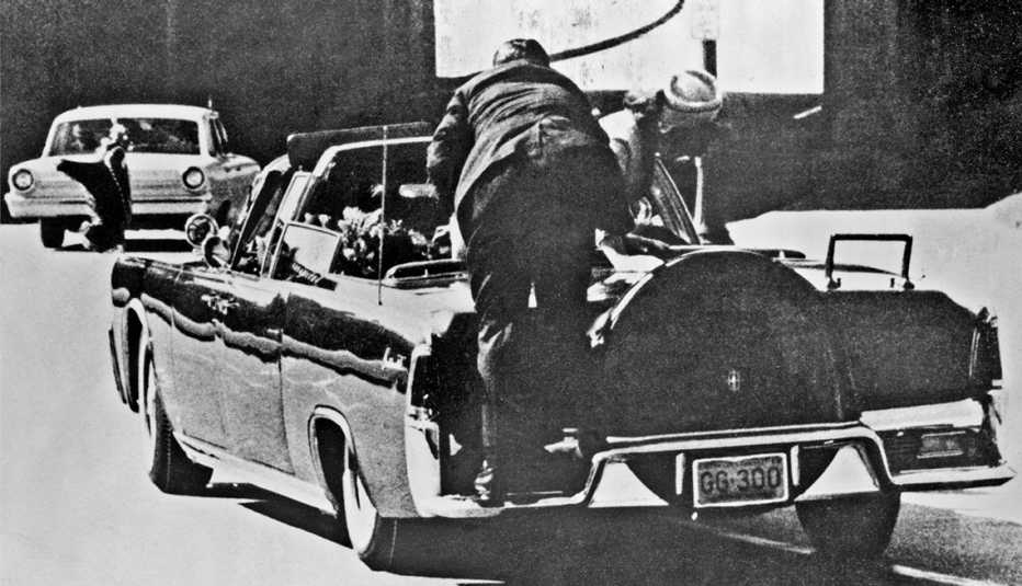 image from the assassination of president john f kennedy showing secret service agent clint hill jumping onto the back of the convertible limousine and jacqueline kennedy leaning over john