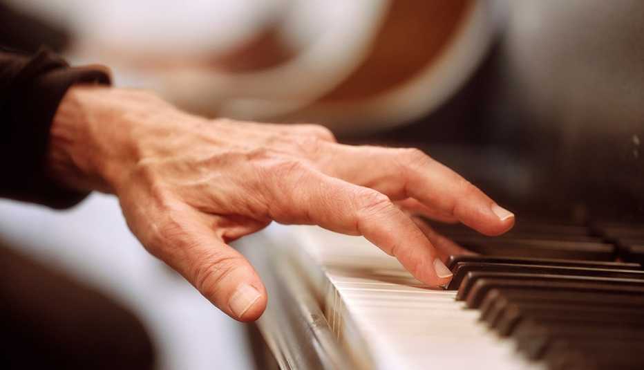 an older persons right hand playing on the keys of a piano 