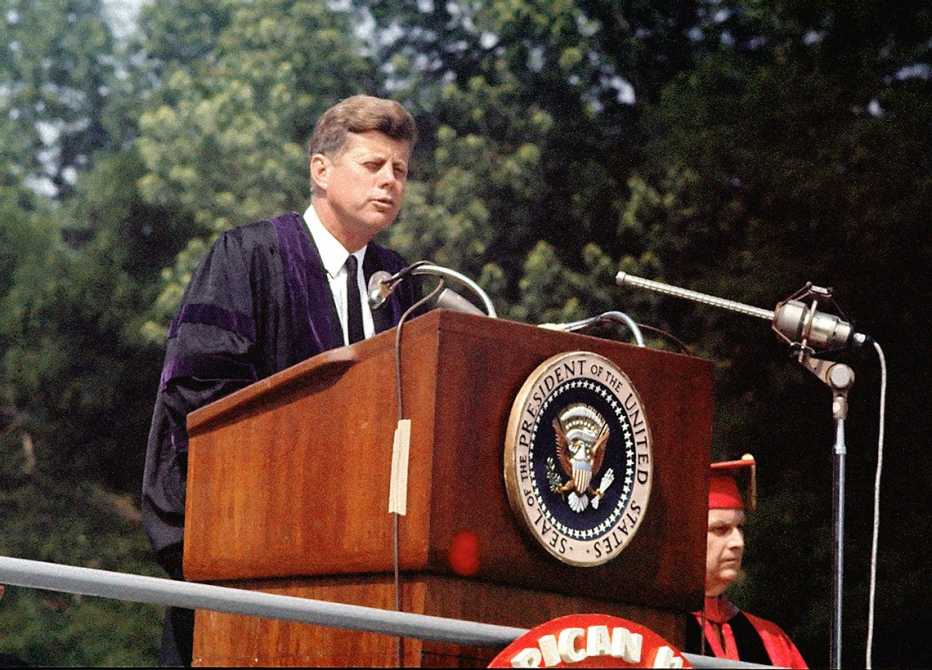 president john f kennedy at a podium outdoors giving his pax americana speech at the nineteen sixty three american university commencement