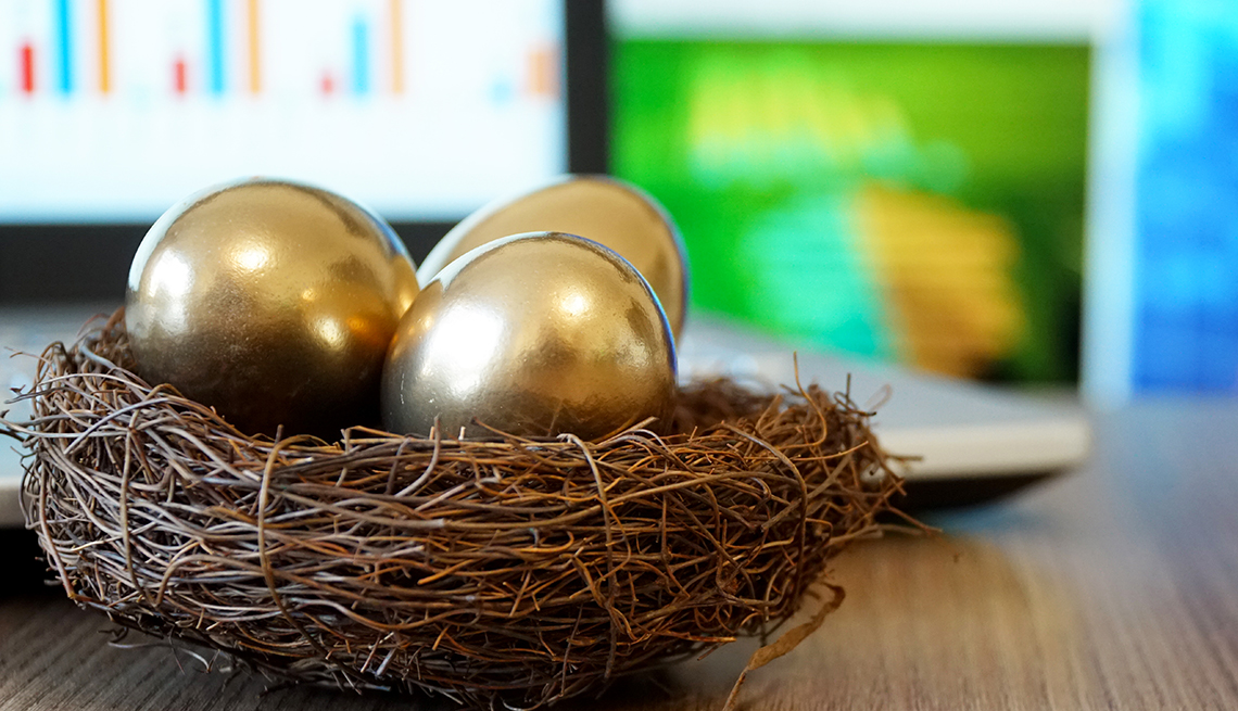 a basket of golden nest eggs in front of soft focus investment screens on computers 