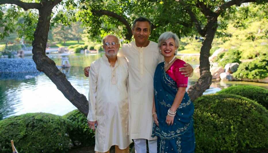three smiling people standing in a garden in front of a pond