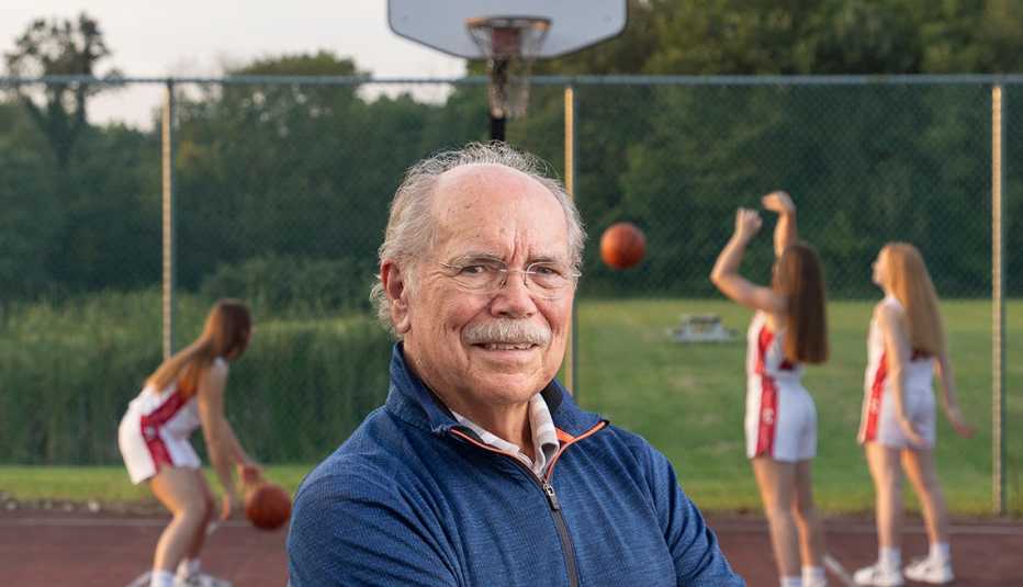sportswriter dave kindred stands on an outdoor basketball court with members of the lady potters team practicing behind him