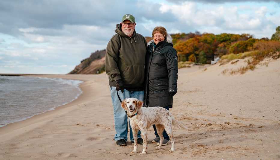 steve and jackie huffstutler standon the beach of lake michigan with their dog dressed in coats during the fall