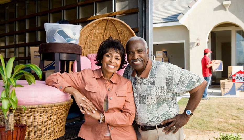 older couple standing with their moving truck smiling 