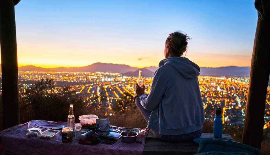 a woman sitting and drinking overlooking santiago and the mountains at sunset in chile