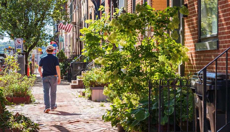 A man in a baseball cap walks down a street filled with charming brick row houses
