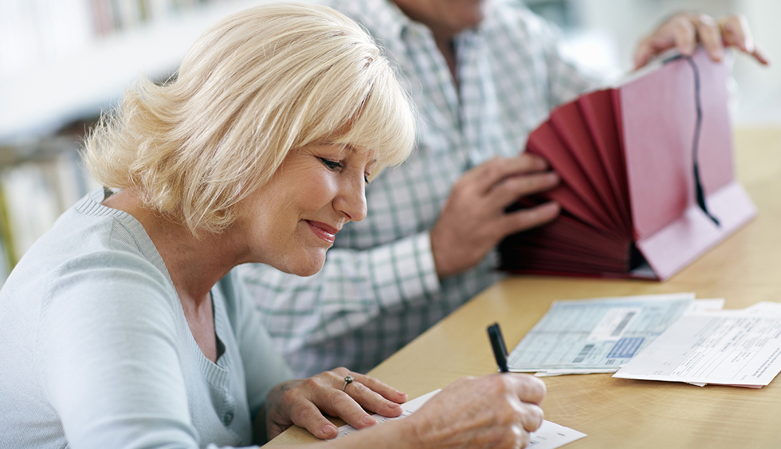 smiling woman in forground writing on financial document while in soft focus background a man is looking through a red accordian style home office file folder 