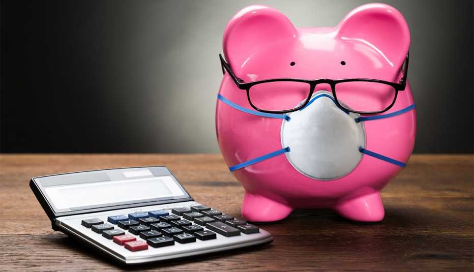 pink piggybank wearing eyeglasses and safety face mask with with calculator on wooden table