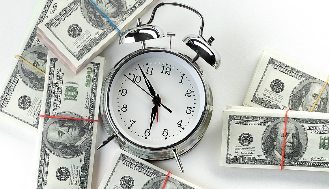 A shiny metal alarm clock surrounded by bundles of U.S. cash