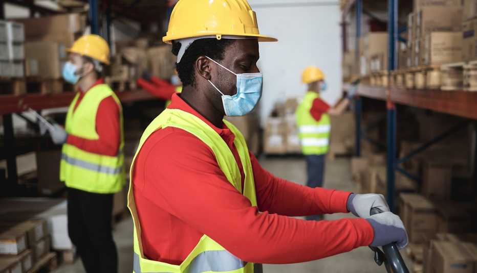 Three warehouse workers wearing red shirts and safety gear  at work in an aisle of  inventory shelves.