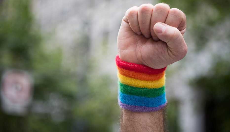Man raises a fist with a pride wristband around his wrist