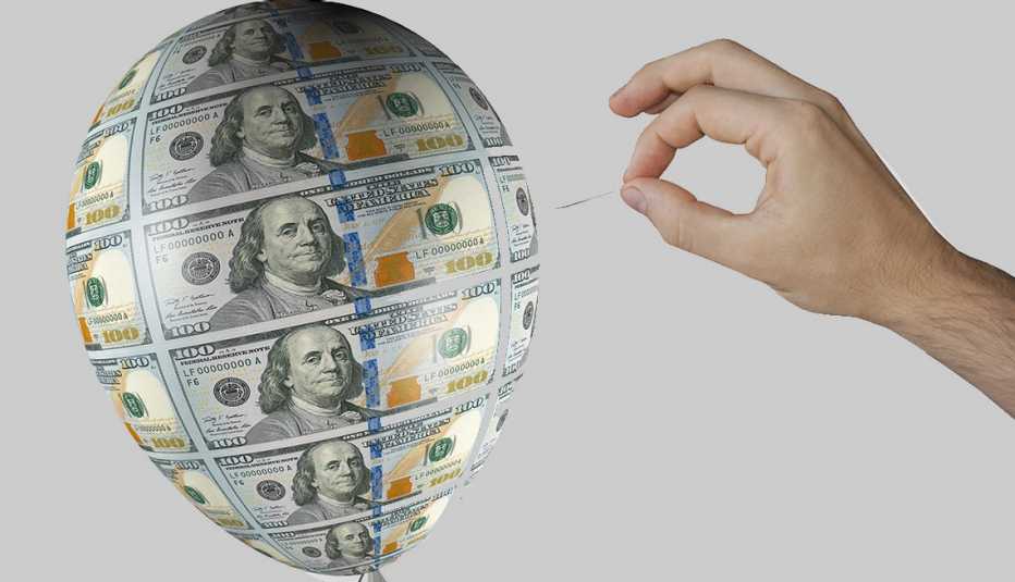 hand holding a pin near an inflated money balloon