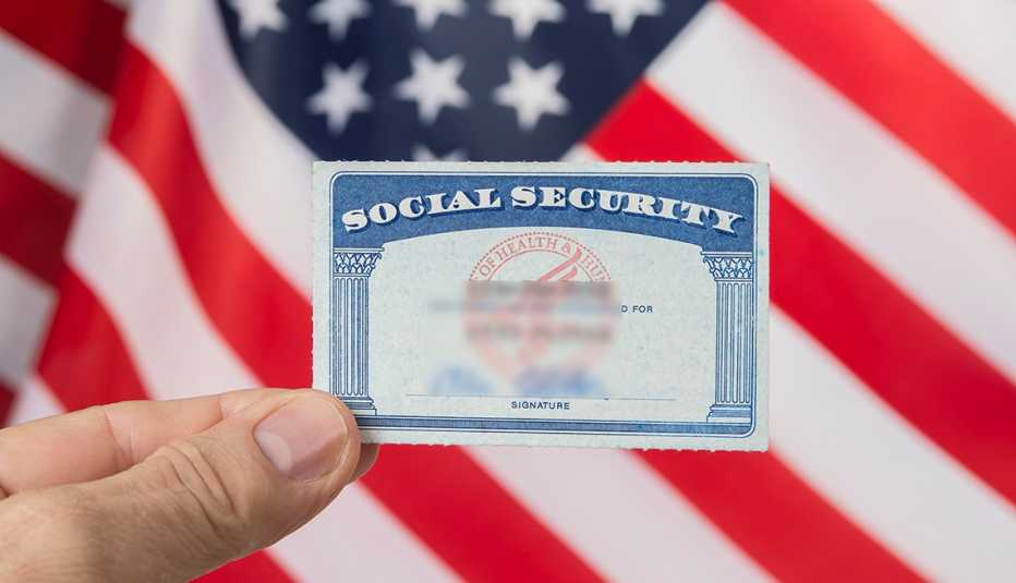 hand holding a social security card above a u s flag background