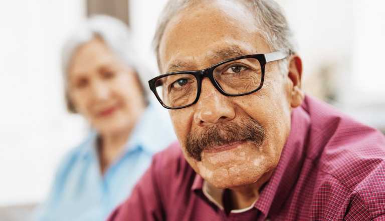 Senior man sitting and wearing glasses and red shirt next to senior woman