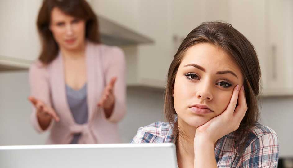 exasperated looking teen with laptop in foreground with concerned or nagging mom in background