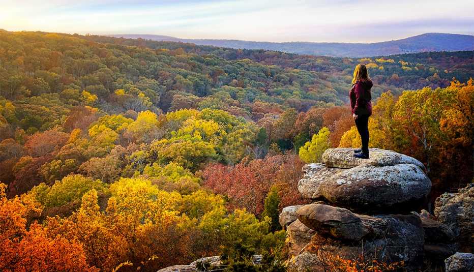 a woman stands on rock in shawnee national forest in illinois surrounded by fall trees