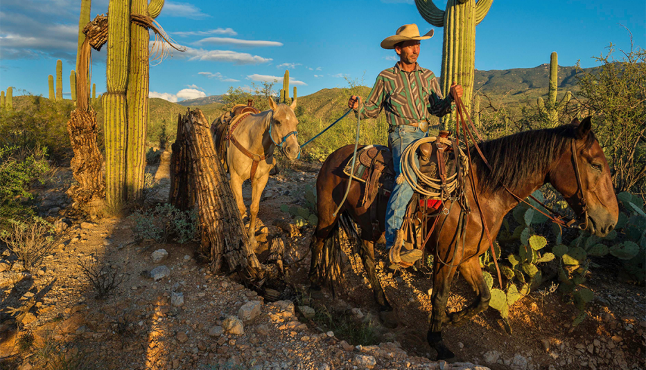 a man riding and leading a horse through cacti at saguaro national park arizona