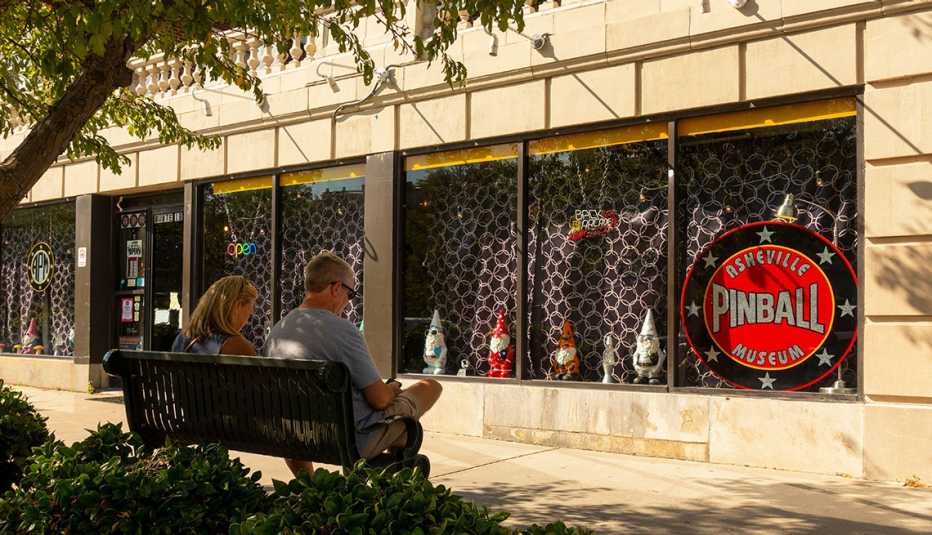 a man and a woman sit on a bench outside the asheville pinball museum storefront