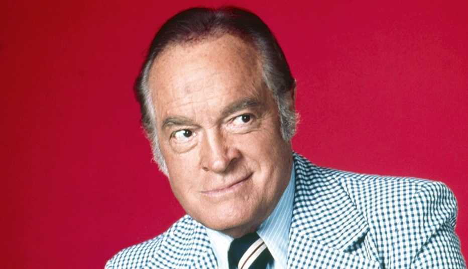 bob hope smiles and looks out of the corner of his eye on a red background