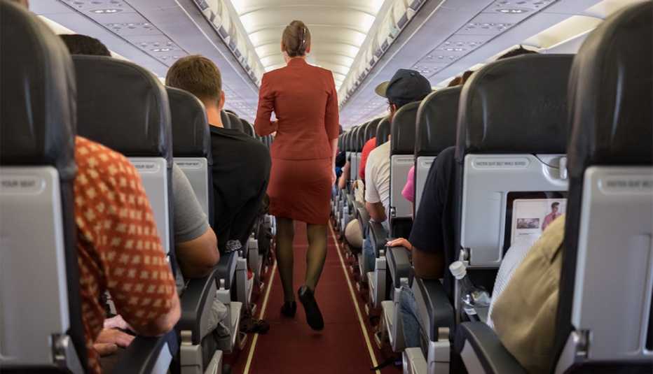 flight attendant walks aisle on airplane with passengers seated