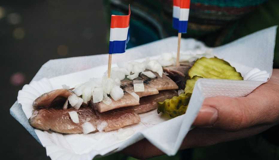 A hand holds a traditional Dutch delicacy of herring with gherkins and onions.