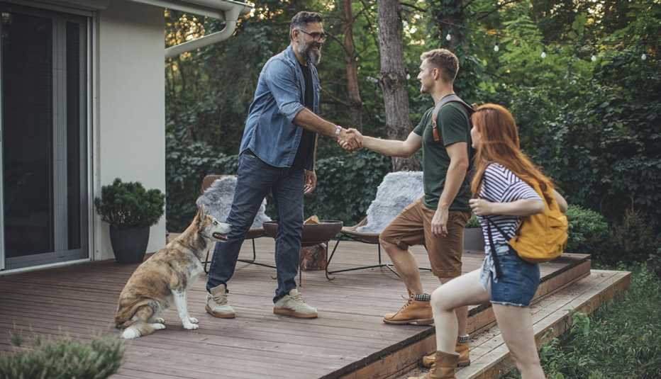 man greeting young couple on the porch of his home and shaking hands with one of them