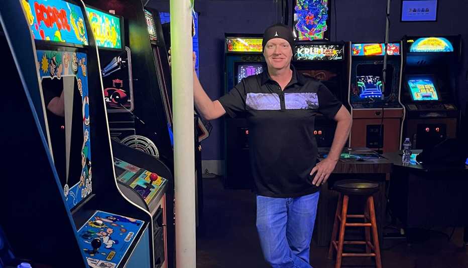 scott leftwich standing next to some arcade games in his eighties style arcade he built in his basement