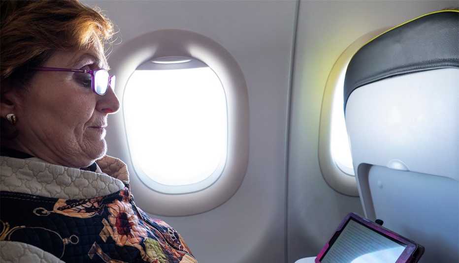 Female airline passenger sitting in a window seat, looking at tablet