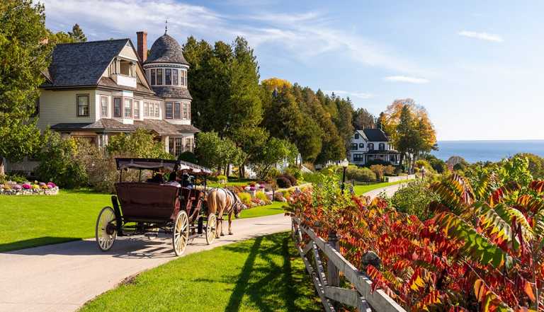 a horse-drawn carriage passes by a historic home on mackinac island in michigan
