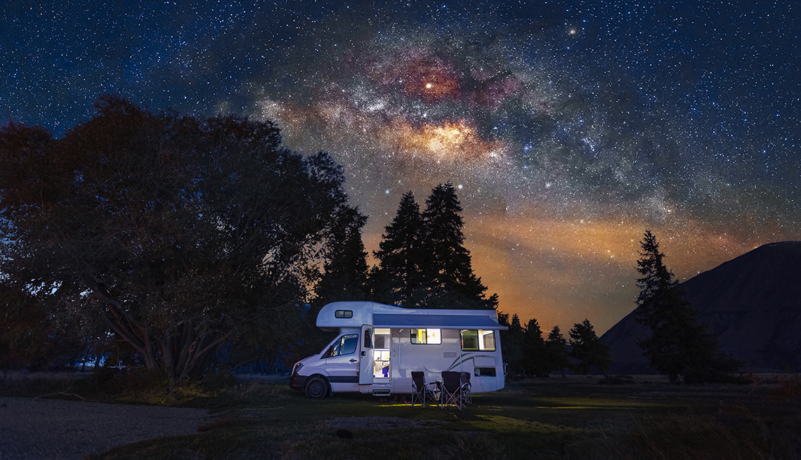 an rv lit up at night under a starry sky with trees in the background